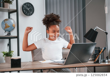 Celebrating success. Passes the exam. Cute female african american student child is sitting by the laptop 125082654