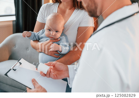 With a prescription. Male doctor is taking care of woman's newborn baby indoors With a prescription. Male doctor is taking care of woman's newborn baby indoors 125082829