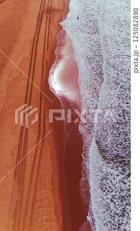 Overhead Drone View of Ocean Waves and Tire Tracks on Red-Toned Beach Overhead Drone View of Ocean Waves and Tire Tracks on Red-Toned Beach 125082890