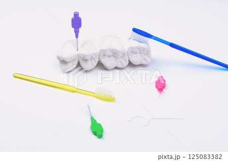 Plaster teeth model with colorful interdental brushes and dental floss around on white background Plaster teeth model with colorful interdental brushes and dental floss around on white background 125083382