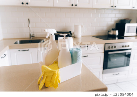 Modern kitchen with cleaning supplies on countertop: gloves, sprays, soap in white minimalist home environment 125084004