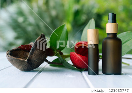Two elegant cosmetic bottles with a pipette are placed on a wooden surface surrounded by greenery. 125085777