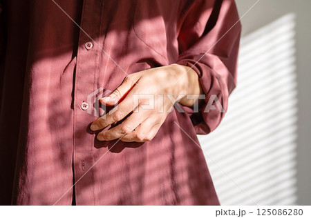 Females Hand Resting on Her Vintage Burgundy Shirt Dappled with Window Light. Fashion Design Blogs or Apparel Advertisements. 125086280