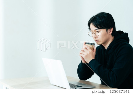 コーヒーを飲みながらパソコンを見る若い男性 コーヒーを飲みながらパソコンを見る若い男性 125087141