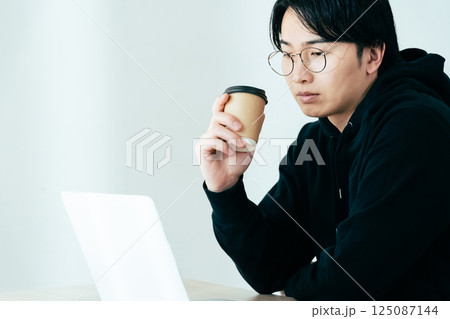 コーヒーを飲みながらパソコンを見る若い男性 コーヒーを飲みながらパソコンを見る若い男性 125087144