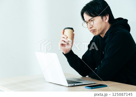 コーヒーを飲みながらパソコンを見る若い男性 125087145