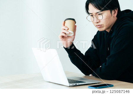 コーヒーを飲みながらパソコンを見る若い男性 コーヒーを飲みながらパソコンを見る若い男性 125087146