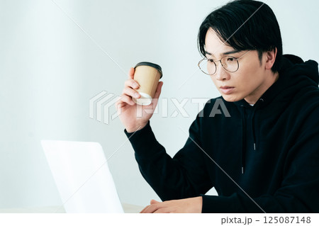 コーヒーを飲みながらパソコンを見る若い男性 125087148