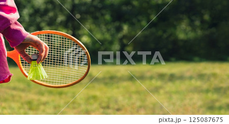 Female hand holding Neon yellow badminton shuttlecock and wooden racket outdoors. Copy space soft selective focus on shuttlecocks. Alternative fitness recreational 125087675