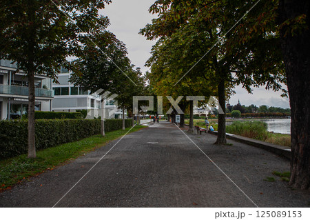 Exploring the serene pathway along Bodensee adorned with trees and charming buildings under a cloudy sky Exploring the serene pathway along Bodensee adorned with trees and charming buildings under a cloudy sky 125089153