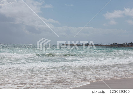 Waves gently lap the shore at Ayia Napa, Cyprus, under a sunny sky filled with distant clouds 125089300