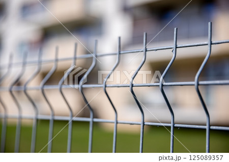 A detailed closeup view of a wavy security fence with a building in the background visible 125089357