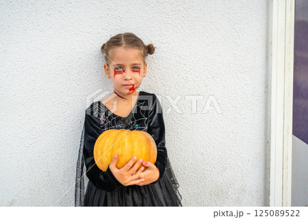 Girl in Halloween makeup holding pumpkin 125089522