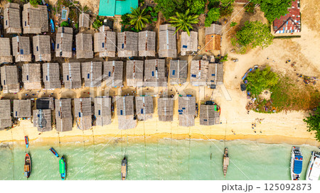 A stunning aerial view of a tropical beach village with rows of small huts along the coastline, 125092873