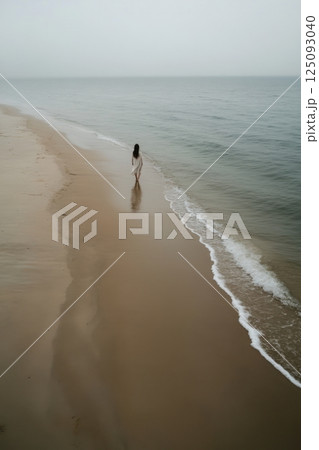 Woman walking alone on a misty beach during a tranquil morning 125093040