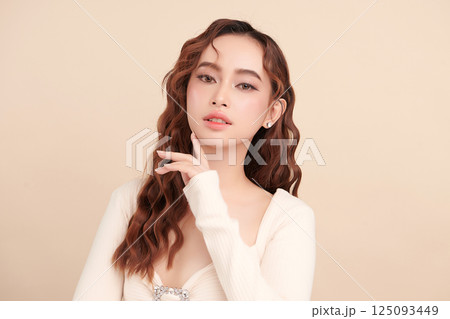 A beautiful young Asian woman with clean, fresh skin against a beige background. Skincare, facial treatment, cosmetology, beauty, and spa. An elegant portrait of an Asian woman. 125093449