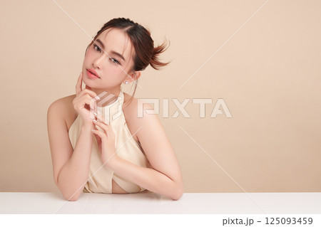A beautiful young Asian woman with clean, fresh skin against a beige background. Skincare, facial treatment, cosmetology, beauty, and spa. An elegant portrait of an Asian woman. 125093459