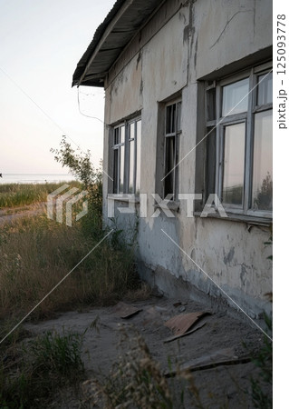 Abandoned rural house surrounded by tall grassy fields and wooden debris 125093778