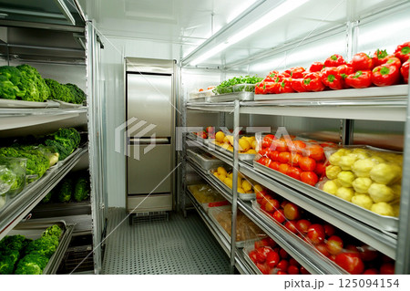 An open refrigerator filled with fresh food items, including ripe tomatoes, lemons, and leafy greens, neatly arranged on the shelves. healthy eating, kitchen organization, and food preservation 125094154