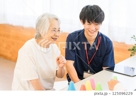リハビリ施設,介護施設で働く若いアジア人男性スタッフとシニア女性 リハビリ施設,介護施設で働く若いアジア人男性スタッフとシニア女性 125096229