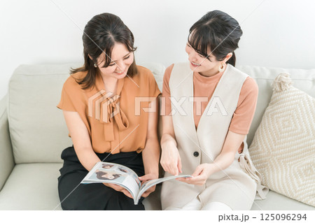 ファッション雑誌,カタログを女友達と一緒におしゃべりしながら見るアジア人女性 125096294