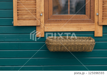 Empty Wicker Flowerpot Hanging Under The Window Of A Wooden House, Exterior Design Empty Wicker Flowerpot Hanging Under The Window Of A Wooden House, Exterior Design 125096593