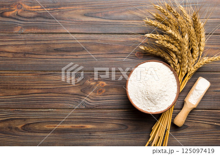 Flat lay of Wheat flour in wooden bowl with wheat spikelets on colored background. world wheat crisis Flat lay of Wheat flour in wooden bowl with wheat spikelets on colored background. world wheat crisis 125097419