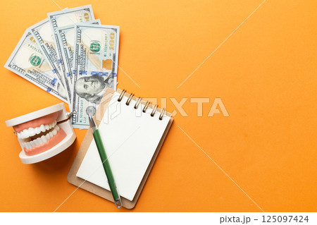 Flat lay composition with educational dental typodont model and money with notebook on colored table, top view. Expensive treatment 125097424