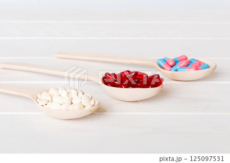 Vitamin capsules in a spoon on a colored background. Pills served as a healthy meal. Red soft gel vitamin supplement capsules on spoon 125097531