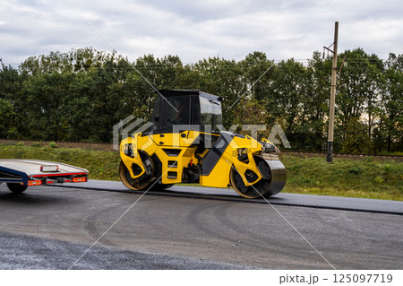 Heavy asphalt road roller that press new hot asphalt on the roadway on a road construction site on a street. 125097719