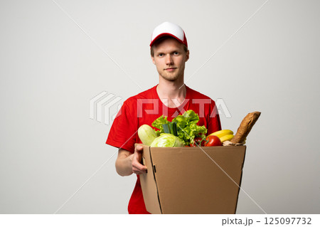 Deliver man wearing red uniform handling bag of food, fruit, vegetable. Postman and express grocery delivery service. 125097732