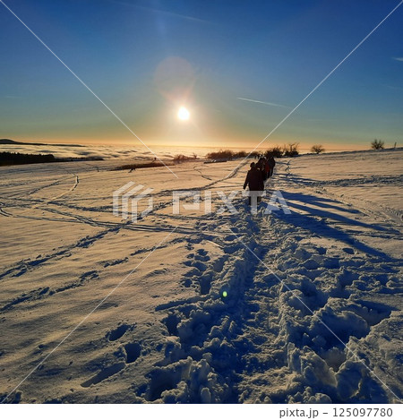 The concept of relaxing in the mountains in winter in the snow on skis, snowboards or sleds, walking under the setting sun at sunset on the Wasserkuppe mountain in Hesse Germany The concept of relaxing in the mountains in winter in the snow on skis, snowboards or sleds, walking under the setting sun at sunset on the Wasserkuppe mountain in Hesse Germany 125097780