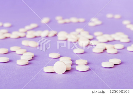 Heap of white pills on colored background. Tablets scattered on a table. Pile of red soft gelatin capsule. Vitamins and dietary supplements concept 125098103