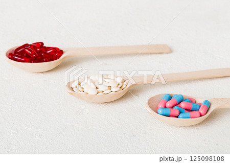 Vitamin capsules in a spoon on a colored background. Pills served as a healthy meal. Red soft gel vitamin supplement capsules on spoon 125098108