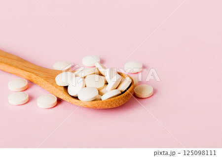 Heap of white pills on colored background. Tablets scattered on a table. Pile of red soft gelatin capsule. Vitamins and dietary supplements concept Heap of white pills on colored background. Tablets scattered on a table. Pile of red soft gelatin capsule. Vitamins and dietary supplements concept 125098111