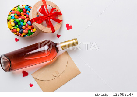 Bottle of red wine on colored background for Valentine Day with gift and chocolate. Heart shaped with gift box of chocolates top view with copy space 125098147