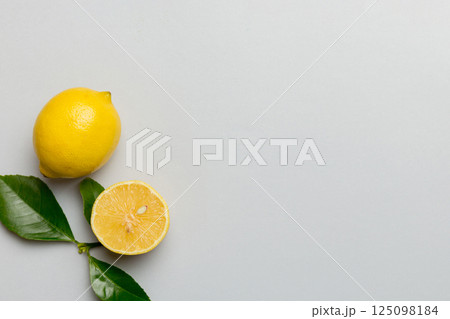 Many fresh ripe lemons with green leaves on colored background, top view, space for text 125098184