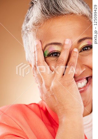 Makeup, comic and senior woman creative with color for face against a brown studio background. Playful, happy and hand of an elderly model with facial cosmetics for creativity, beauty and fashion Makeup, comic and senior woman creative with color for face against a brown studio background. Playful, happy and hand of an elderly model with facial cosmetics for creativity, beauty and fashion 125099429
