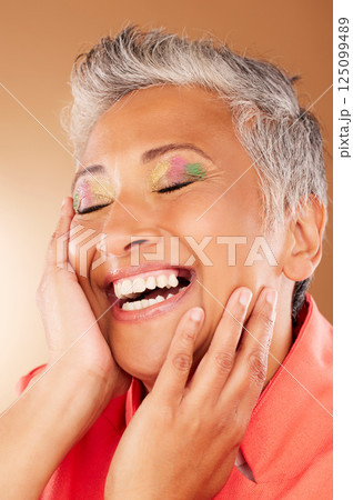 Happy, color and senior woman with makeup standing in a studio with colorful, trendy and edgy cosmetics. Happiness, smile and elderly lady with a beauty routine isolated by gradient brown background. 125099489