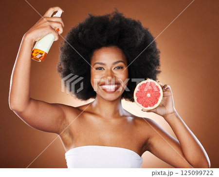 Grapefruit, black woman and afro hair spray, beauty and serum in hair care maintenance, aesthetic wellness or natural cosmetics on studio background. Portrait african model, citrus oil and curly hair 125099722