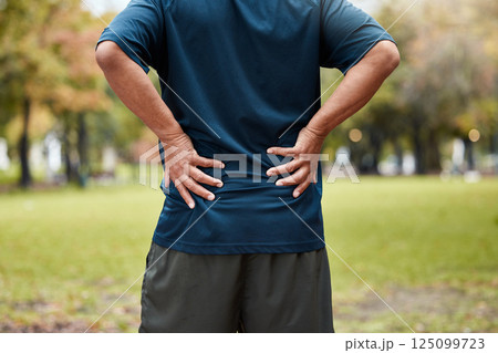 Exercise, fitness and back pain of man at park after workout. Break, healthcare or mature male runner with back injury, muscle pain and inflammation after exercising, running or training in nature 125099723