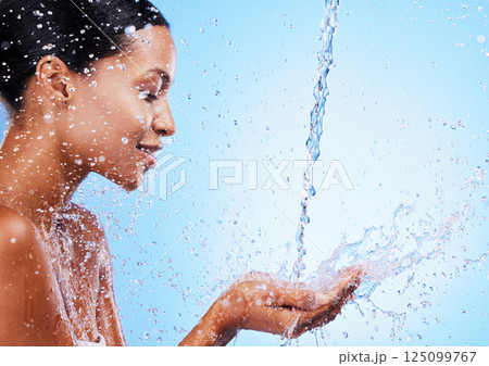 Water, splash and black woman doing skincare for health, wellness and hygiene in a studio. Beauty, shower and girl model doing a natural treatment for skin, body or face with aqua by blue background. 125099767