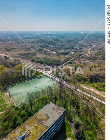 Aerial view of a football field near a building, surrounded by trees and trails, with vast open hills and distant cityscape under a clear blue sky. Aerial view of a football field near a building, surrounded by trees and trails, with vast open hills and distant cityscape under a clear blue sky. 125099863