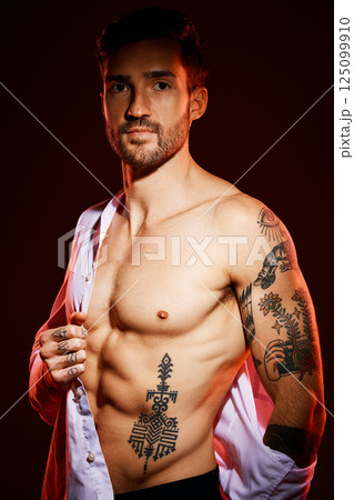 Fashion, sexy and portrait of a man in a studio with muscles, body and tattoos for body care or fitness. Handsome, young and edgy model from Canada posing with bare chest isolated by dark background. Fashion, sexy and portrait of a man in a studio with muscles, body and tattoos for body care or fitness. Handsome, young and edgy model from Canada posing with bare chest isolated by dark background. 125099910