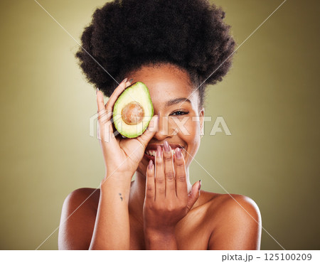 Black woman, laughing or avocado skincare on green studio background for healthcare diet, dermatology wellness or nutrition. Portrait, smile or happy beauty model with fruit as organic facial product 125100209