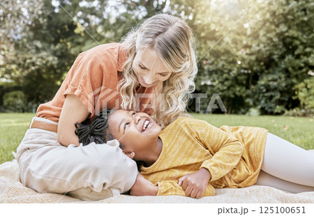 Happy family, interracial and girl and mother relax in a park, happy and smile while resting on grass together. Love, family and black child laughing with her mom, cheerful and peaceful in a yard 125100651