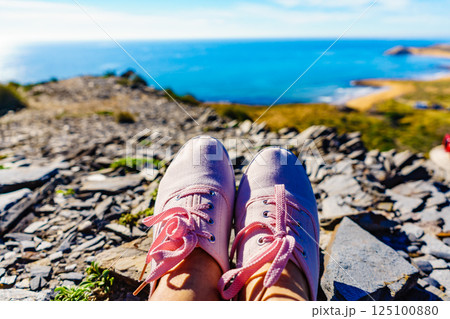Female legs in sneakers against coast landscape, Spain. 125100880