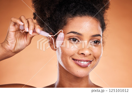 Smile facial beauty, black woman with roller for happy wellness, aesthetic or health makeup, glowing skin on orange studio background. Girl, model or face massage for skincare cosmetics or healthcare 125101012