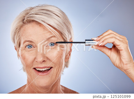 Portrait of senior woman with mascara brush, cosmetic beauty product and makeup wand for eye lashes in Sydney. Surprised smile in studio with gray background, natural blue eyes and luxury skincare 125101099