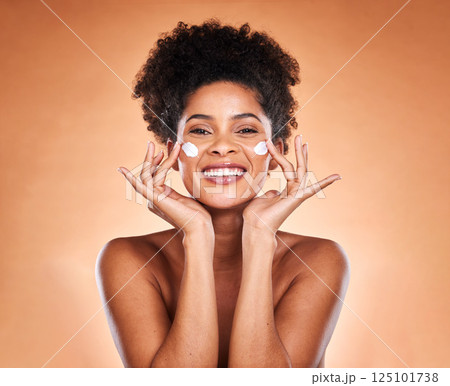 Sunscreen, black woman with skincare product on face and beauty in studio with orange background in Atlanta. Healthy smile for portrait, collagen cream for facial glow or cosmetic lotion for acne 125101738